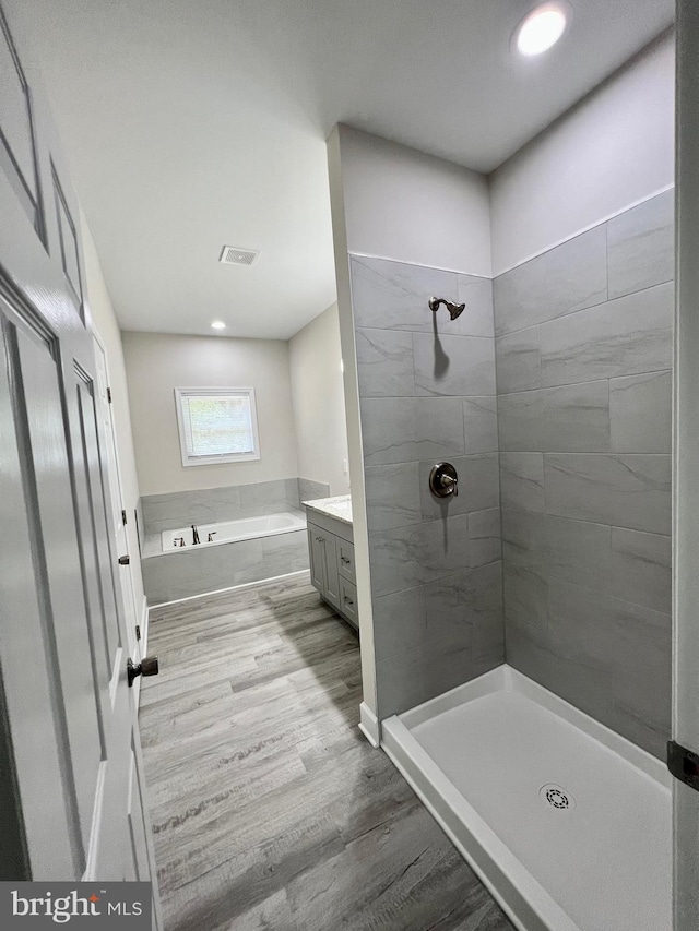 bathroom featuring plus walk in shower, vanity, and wood-type flooring