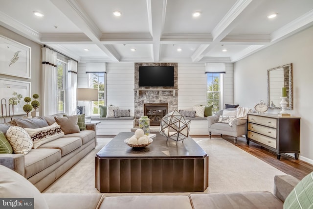 living room featuring ornamental molding, coffered ceiling, beam ceiling, light hardwood / wood-style flooring, and a stone fireplace