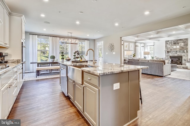 kitchen with a stone fireplace, sink, an island with sink, beamed ceiling, and wood-type flooring