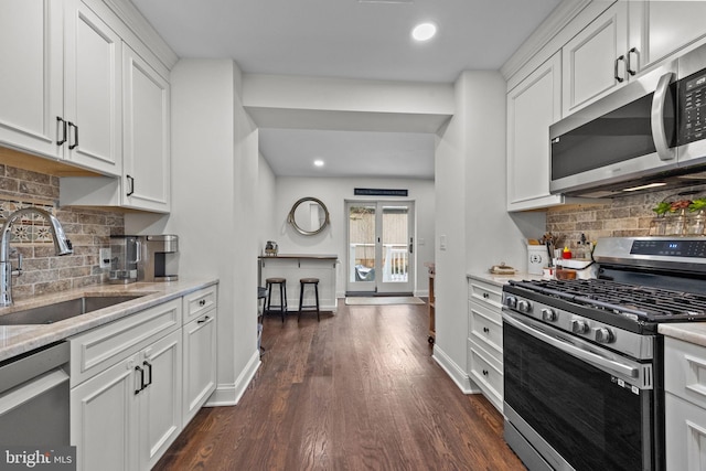 kitchen with dark wood-type flooring, sink, light stone countertops, appliances with stainless steel finishes, and white cabinetry