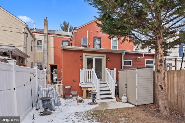 snow covered back of property featuring a shed and central AC