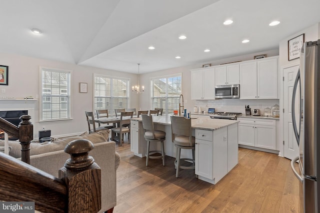 kitchen featuring decorative light fixtures, vaulted ceiling, white cabinetry, a kitchen island with sink, and stainless steel appliances