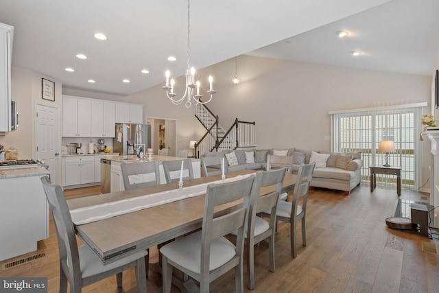 dining area with high vaulted ceiling, wood-type flooring, and a chandelier