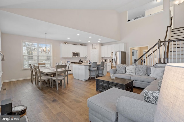 living room with high vaulted ceiling, wood-type flooring, sink, and an inviting chandelier