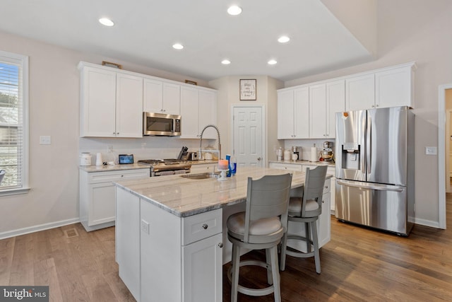 kitchen with white cabinetry, an island with sink, appliances with stainless steel finishes, light stone countertops, and sink