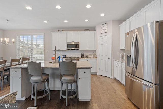 kitchen featuring pendant lighting, white cabinets, stainless steel appliances, and an island with sink