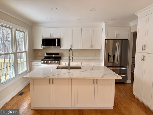 kitchen with stainless steel appliances, an island with sink, light stone countertops, and sink