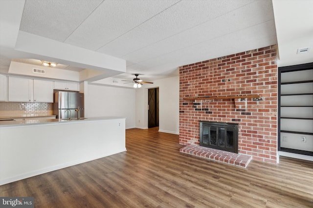 unfurnished living room featuring ceiling fan, wood-type flooring, and a brick fireplace