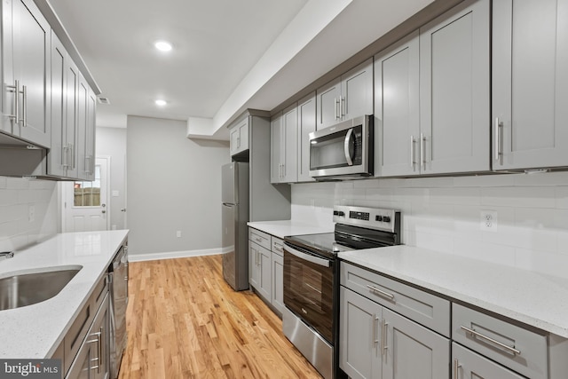 kitchen with sink, light stone counters, light hardwood / wood-style floors, gray cabinets, and appliances with stainless steel finishes