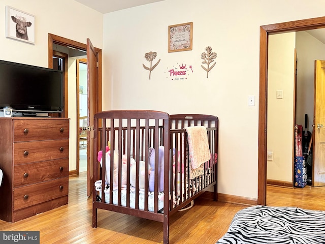 bedroom featuring a nursery area and light hardwood / wood-style floors