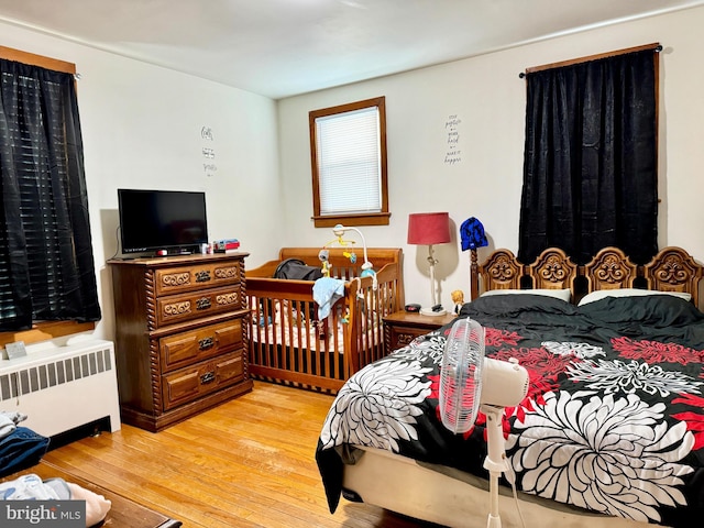 bedroom with a nursery area, light hardwood / wood-style flooring, and radiator heating unit