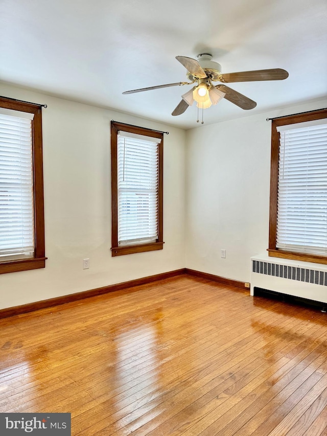 unfurnished room featuring ceiling fan, light wood-type flooring, and radiator heating unit