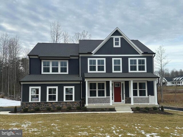 craftsman-style house with stone siding, a porch, board and batten siding, and roof with shingles