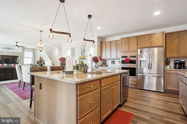 kitchen with stainless steel appliances, wood finished floors, a kitchen breakfast bar, open floor plan, and light stone countertops