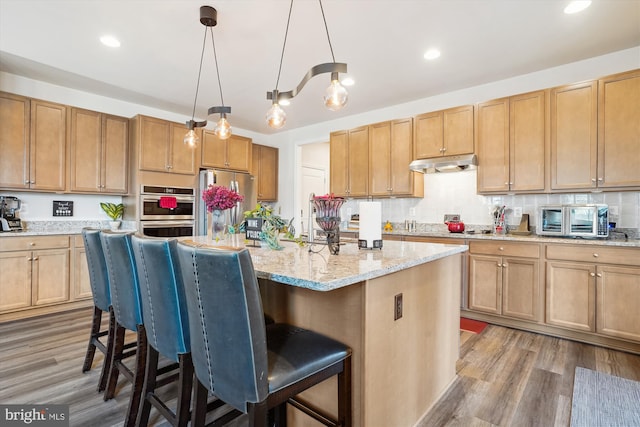 kitchen featuring stainless steel appliances, under cabinet range hood, a kitchen bar, and wood finished floors