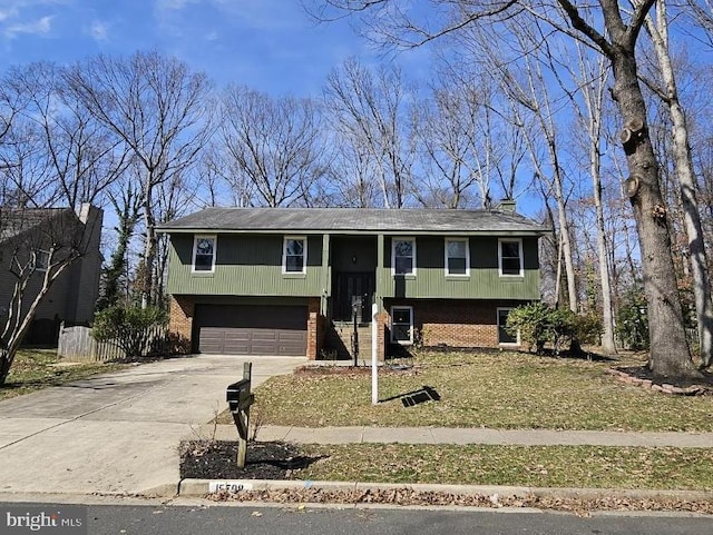 raised ranch featuring a garage, brick siding, driveway, and fence