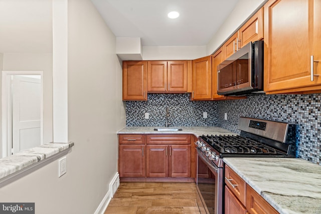 kitchen with light stone countertops, sink, light hardwood / wood-style flooring, decorative backsplash, and appliances with stainless steel finishes