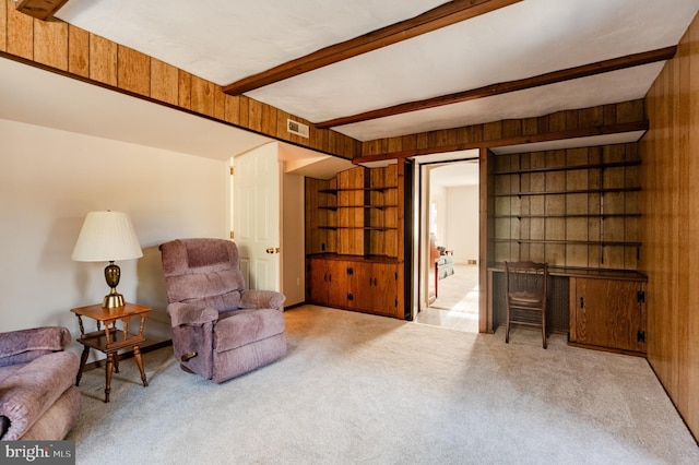 living area featuring wood walls, beamed ceiling, and light carpet