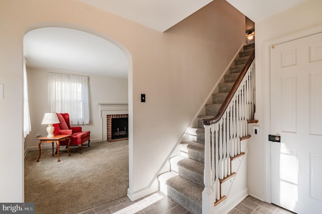 stairs featuring a brick fireplace and carpet floors