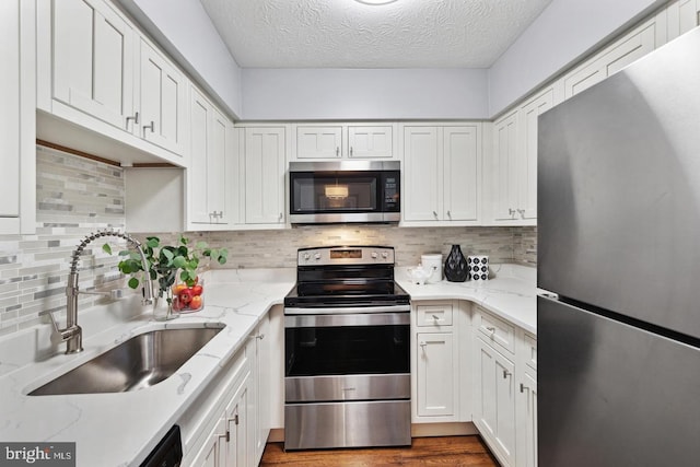 kitchen featuring white cabinets, appliances with stainless steel finishes, light stone countertops, and sink