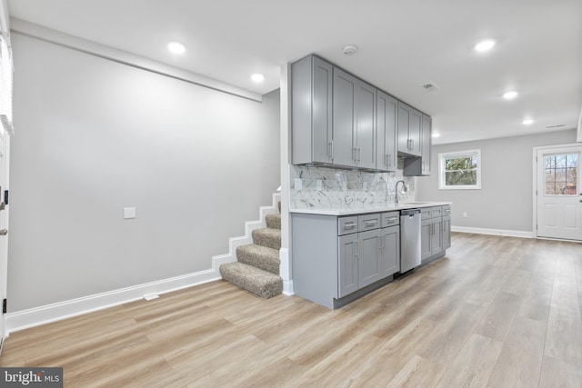 kitchen featuring tasteful backsplash, stainless steel dishwasher, sink, light hardwood / wood-style flooring, and gray cabinets