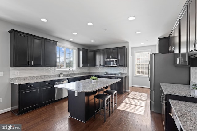 kitchen featuring appliances with stainless steel finishes, dark wood-type flooring, light stone countertops, a kitchen island, and a breakfast bar area