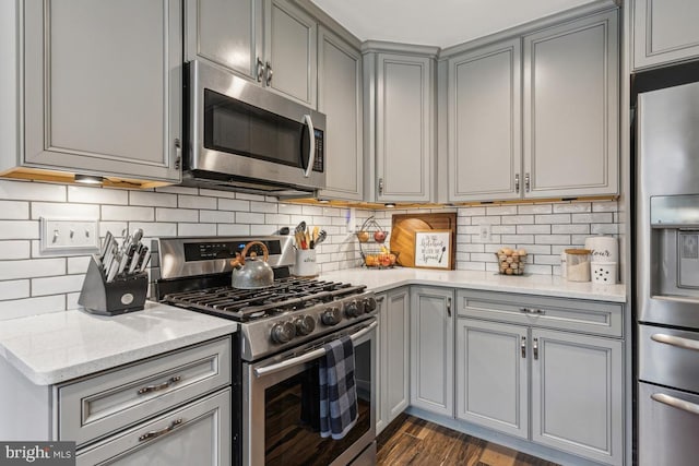 kitchen with stainless steel appliances, light stone counters, gray cabinets, decorative backsplash, and dark hardwood / wood-style floors