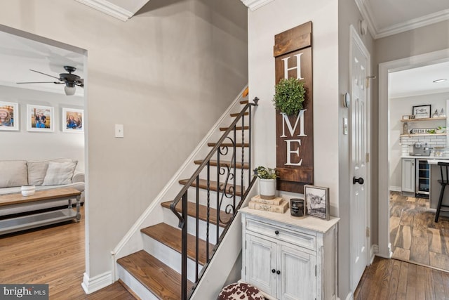 stairway with ceiling fan, beverage cooler, ornamental molding, and hardwood / wood-style flooring