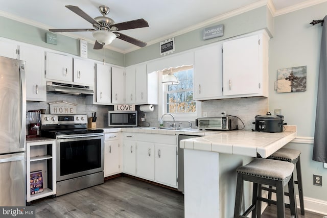 kitchen featuring tile countertops, a kitchen bar, appliances with stainless steel finishes, white cabinets, and sink