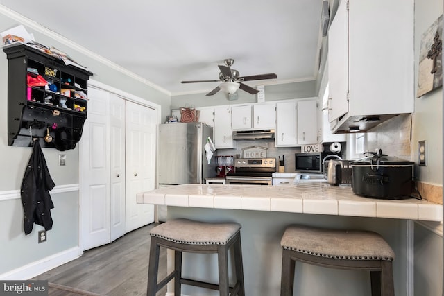 kitchen with a kitchen breakfast bar, tile countertops, stainless steel appliances, and white cabinets