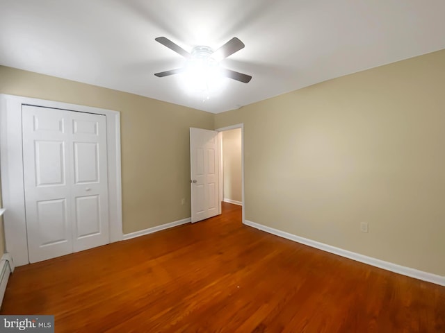 unfurnished bedroom with ceiling fan, wood-type flooring, a baseboard radiator, and a closet