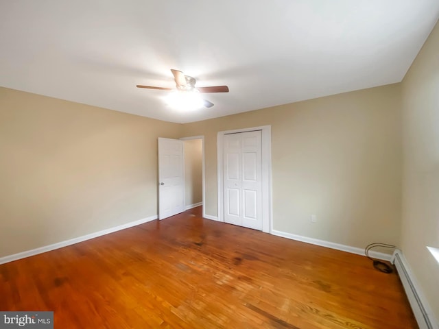 unfurnished bedroom with ceiling fan, a closet, a baseboard heating unit, and hardwood / wood-style flooring