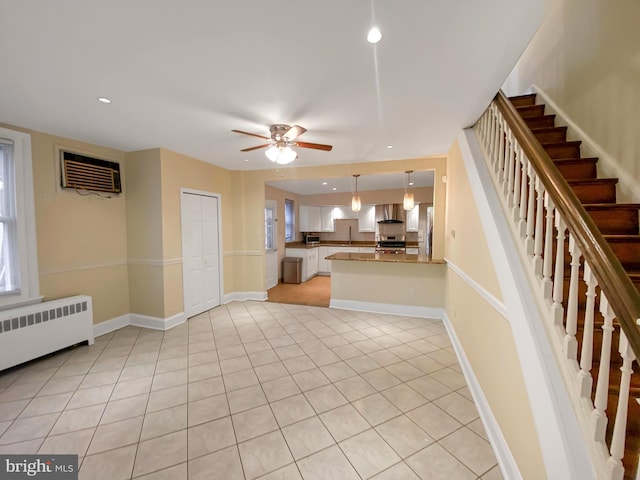 kitchen featuring radiator, wall chimney range hood, a wall unit AC, kitchen peninsula, and appliances with stainless steel finishes