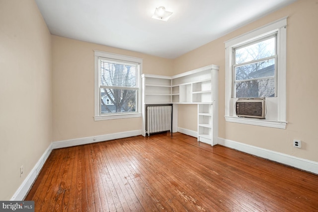 unfurnished bedroom with cooling unit, radiator heating unit, and wood-type flooring