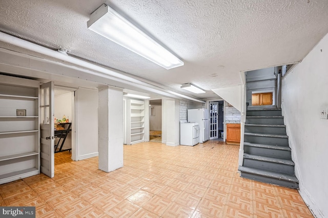 basement featuring white fridge, washing machine and clothes dryer, and a textured ceiling