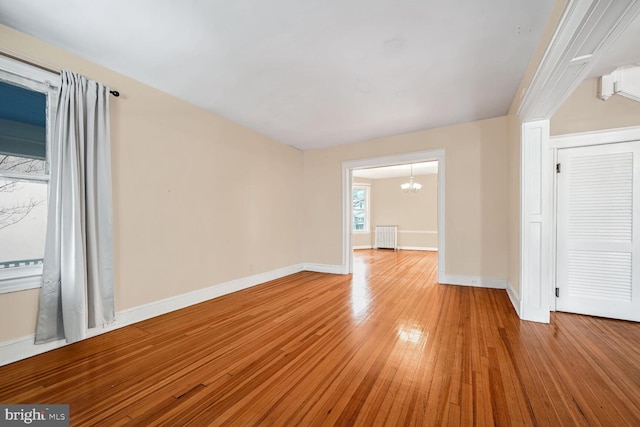 spare room featuring an inviting chandelier, radiator, and light hardwood / wood-style floors