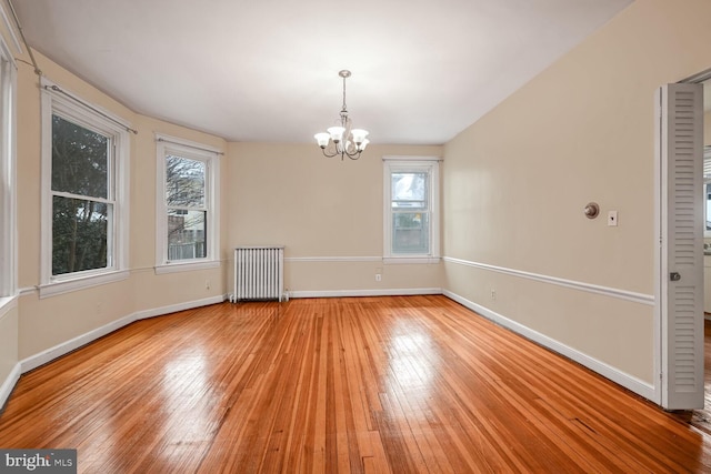 unfurnished dining area with an inviting chandelier, radiator, and light wood-type flooring