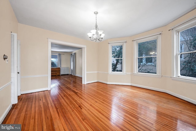 unfurnished dining area featuring hardwood / wood-style flooring, radiator, and a notable chandelier