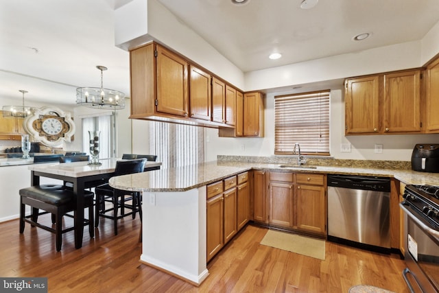 kitchen with appliances with stainless steel finishes, hanging light fixtures, light wood-type flooring, kitchen peninsula, and sink