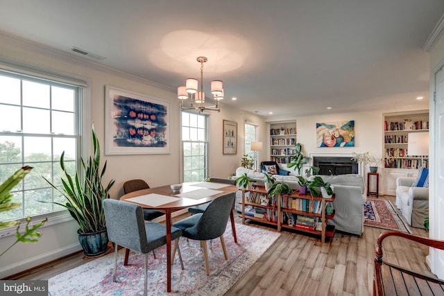 dining room featuring light hardwood / wood-style floors, built in features, crown molding, and an inviting chandelier