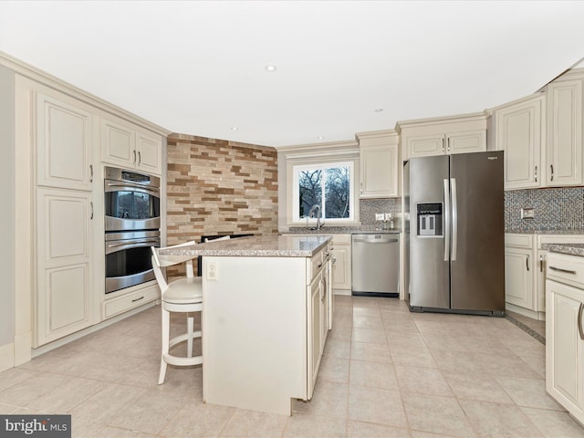 kitchen with appliances with stainless steel finishes, backsplash, cream cabinets, and a kitchen island