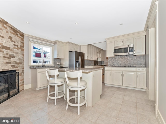 kitchen with appliances with stainless steel finishes, a center island, stone countertops, a breakfast bar, and cream cabinetry