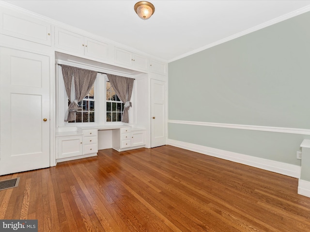 interior space with built in desk, wood-type flooring, and ornamental molding