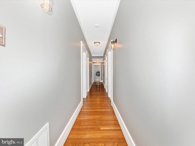 hallway with ornamental molding and light hardwood / wood-style flooring