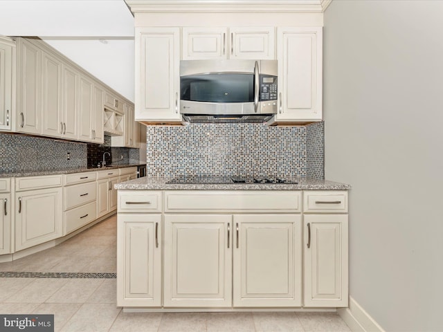 kitchen with light tile patterned floors, cream cabinetry, black electric cooktop, backsplash, and light stone countertops