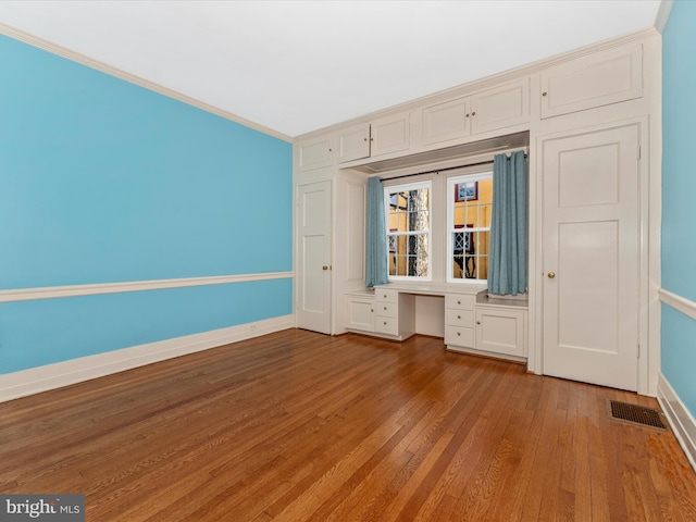 interior space with built in desk, ornamental molding, and light hardwood / wood-style flooring