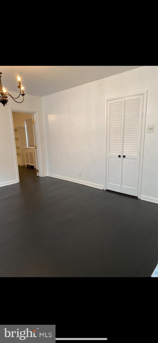 empty room with dark hardwood / wood-style flooring and a chandelier