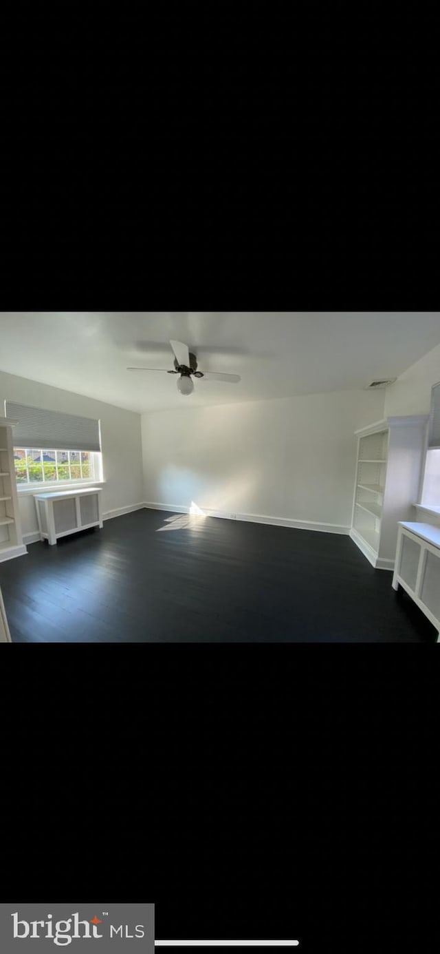 interior space featuring dark hardwood / wood-style flooring, built in shelves, ceiling fan, and a healthy amount of sunlight