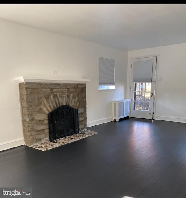 unfurnished living room featuring dark hardwood / wood-style flooring, a fireplace, and radiator