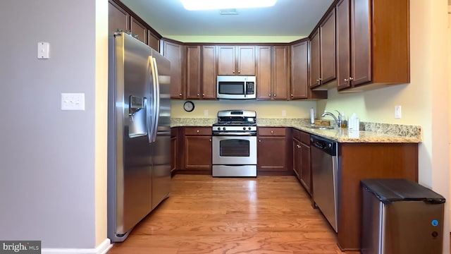 kitchen with appliances with stainless steel finishes, light hardwood / wood-style flooring, light stone counters, and sink